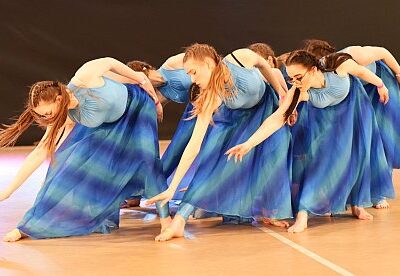Fotografia przedstawia sześć kobiet w pozach tanecznych, ubrane w niebieskie bluzki i spódnice.