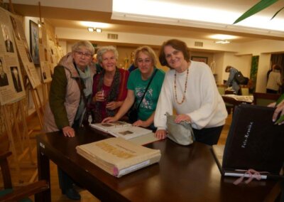 Cztery kobiety z zaciekawieniem spoglądają w stronę fotografa. Na stole leżą przeglądane przez nie kroniki historyczne.