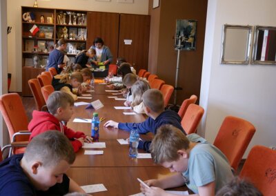 zdjęcie przedstawia grupę dzieci rozwiązujących zagadki przy stołach