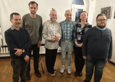 Pamiątkowe zdjęcie po zakończeniu prelekcji w Muzeum Regionalne w Barlinku. W centrum stoi prelegent Grzegorz Przybylski trzymający upominek, obok niego stoją uczestnicy wydarzenia.